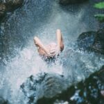 Shower - high-angle photography of woman bathing below waterfalls during daytime
