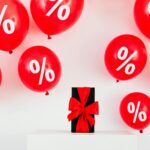 A Gift With Red Ribbon in Between Red Balloons With Percentage Symbols on a White Background